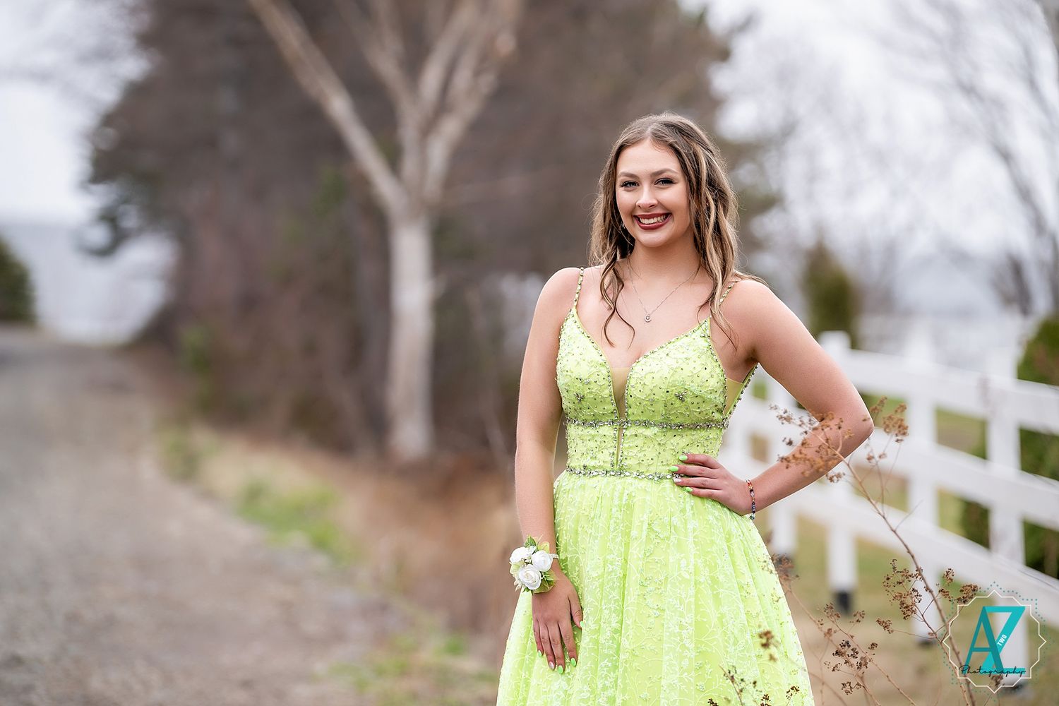 A bright lime green formal dress sparkles against a rustic country path with white fence background.