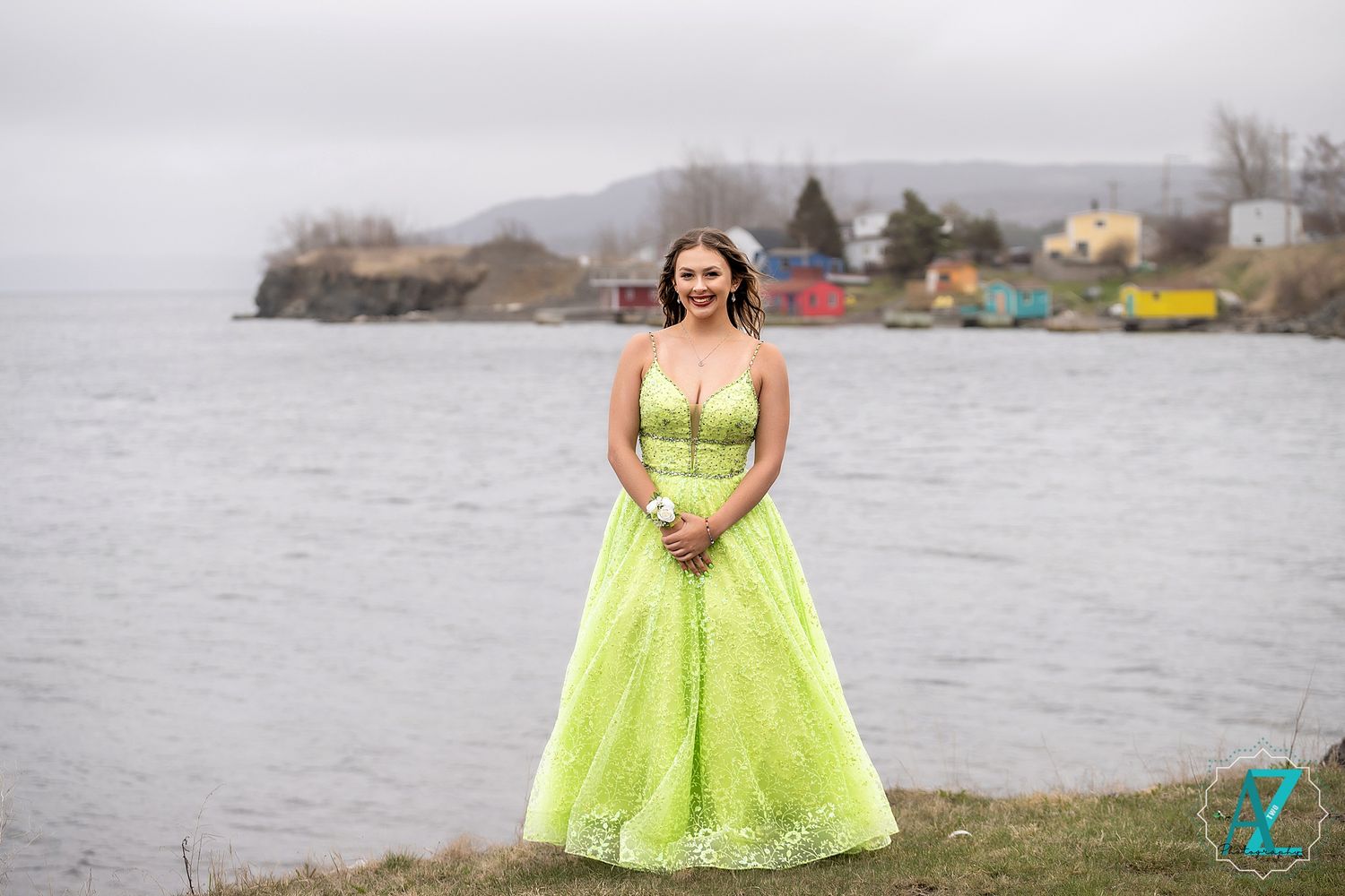 A lime green ball gown creates a striking contrast against a misty coastal landscape with colorful buildings.