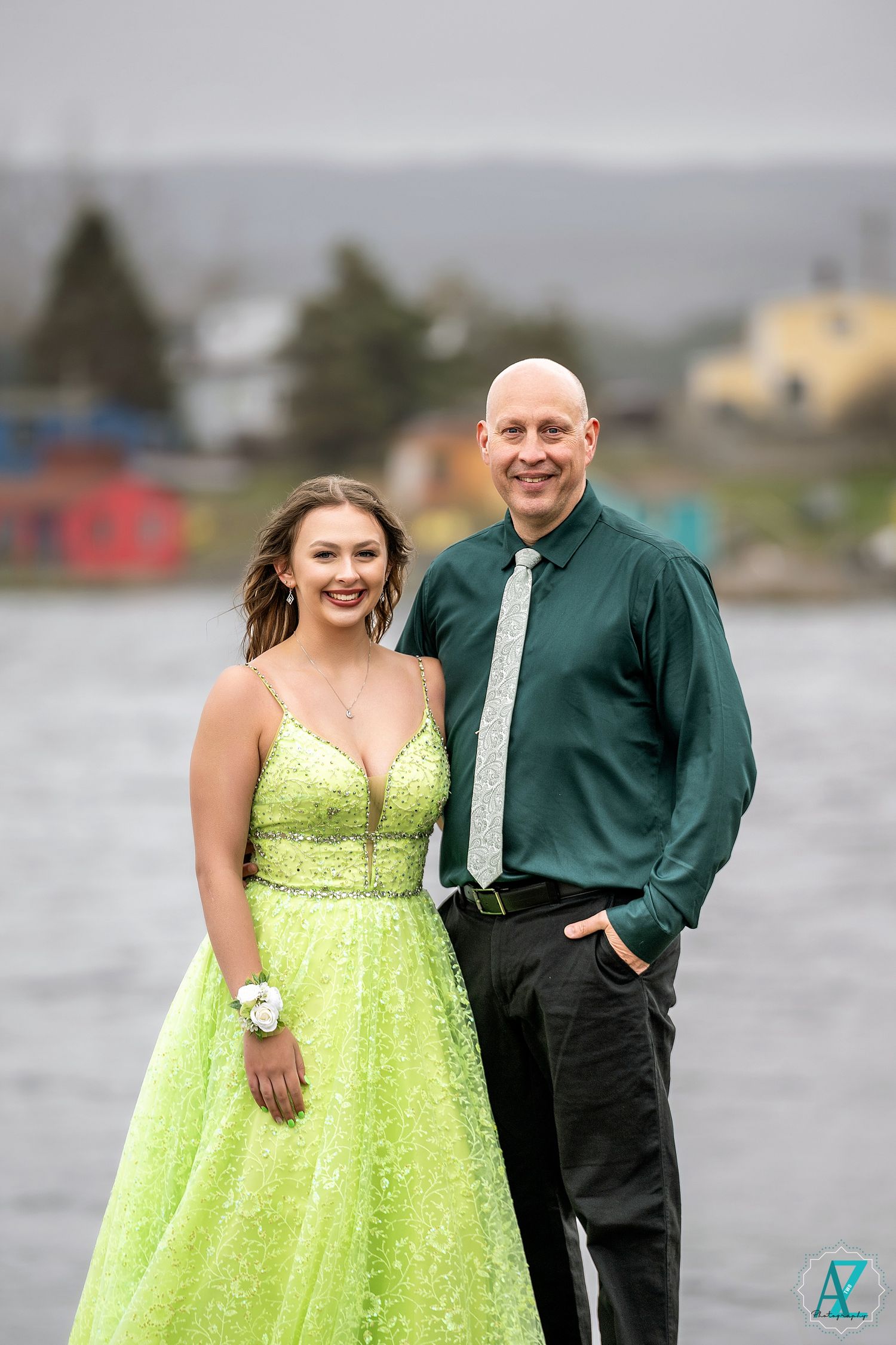 A formal portrait by a lake featuring a sparkling lime green ballgown and dark green formal attire.
