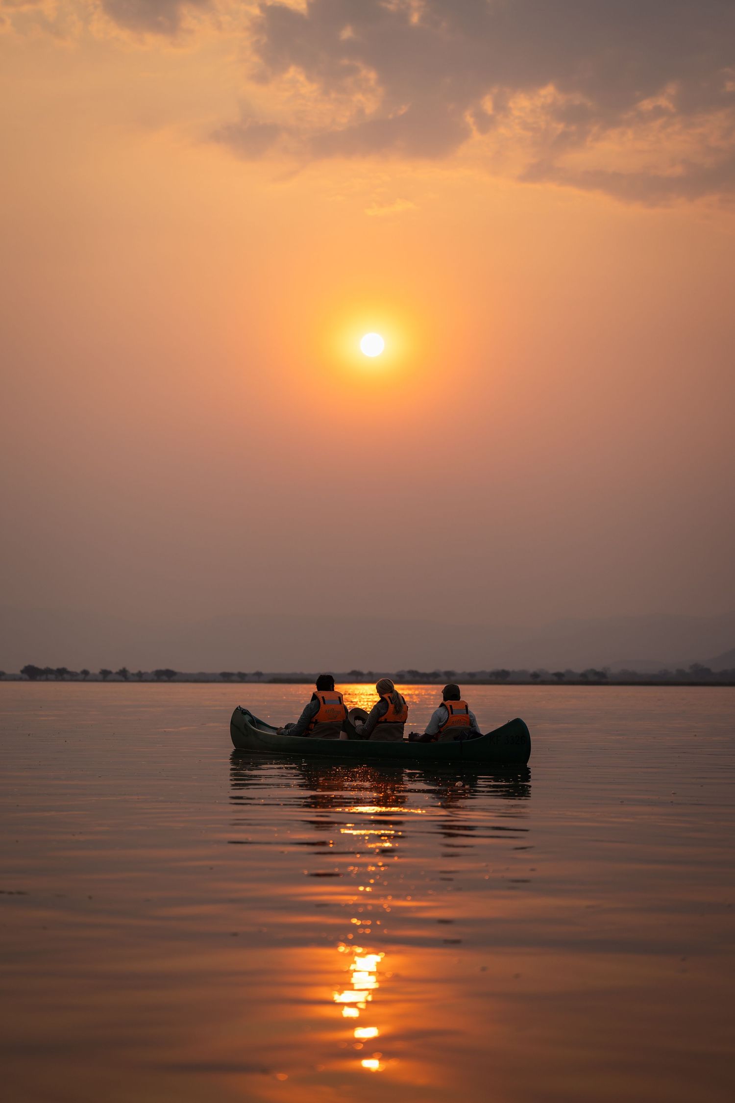 Silhouette of canoe with passengers against dramatic orange sunset over water.
