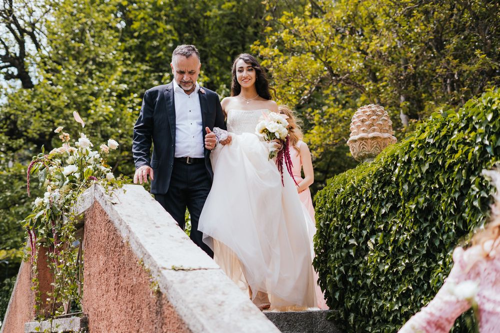 A couple descends elegant stone steps surrounded by lush greenery at an outdoor wedding venue.