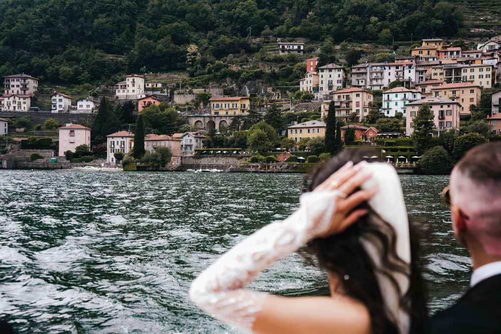 People viewing waterfront buildings on hillside along Lake Como from a boat in Italy.