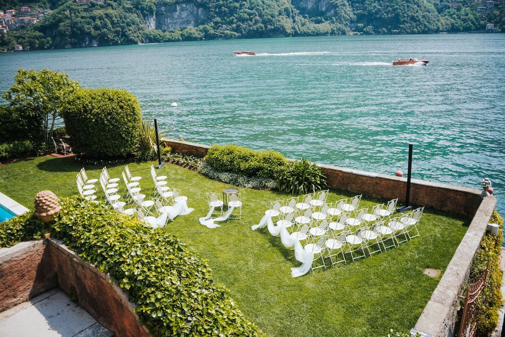 Scenic lakefront wedding venue with white chairs set up on manicured lawn overlooking turquoise waters and mountains.