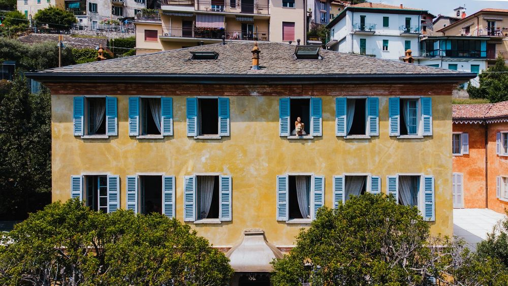 Row of colorful Mediterranean-style buildings with traditional blue shutters and yellow facades line a coastal street.