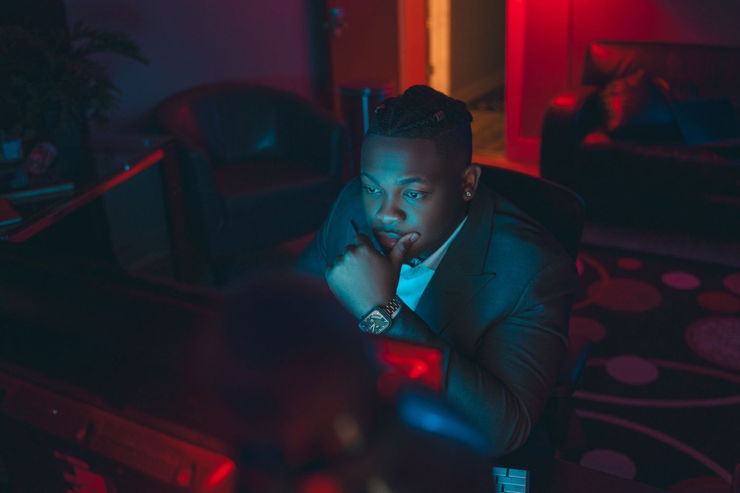 Person illuminated by red and blue lighting sits in atmospheric dark setting.