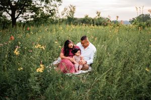 A couple sits together in a field of wildflowers during golden hour with tall grass surrounding them.