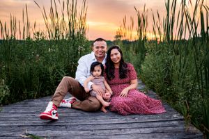 A family sits together on a wooden dock during sunset surrounded by tall grass.