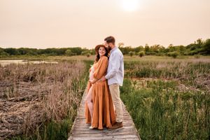 A couple shares a romantic moment on a wooden boardwalk during sunset.
