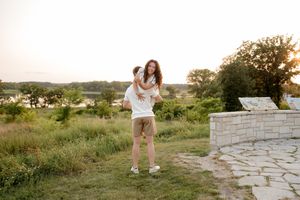 Couple embracing at sunset in a lush green field near a stone wall, sharing a joyful moment outdoors.