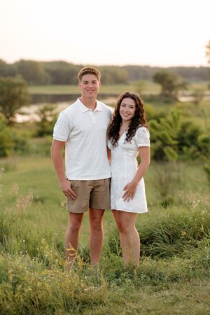 Young couple in white outfits posing together in a lush green field during golden hour sunset.