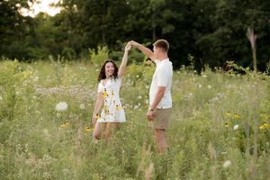 Couple dancing in a wildflower meadow at sunset, woman in white dress, man in white shirt and khaki shorts.