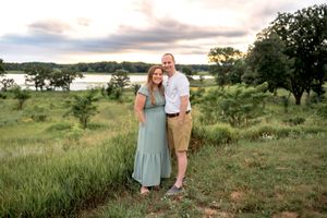 Couple walking hand in hand through lush green meadow during golden sunset hours.