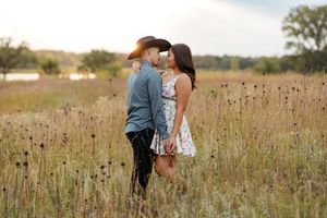 A couple shares an intimate moment in a golden meadow during sunset, surrounded by tall wildflowers and prairie grass.