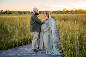 A tender moment captured on a wooden boardwalk surrounded by tall grass at sunset.