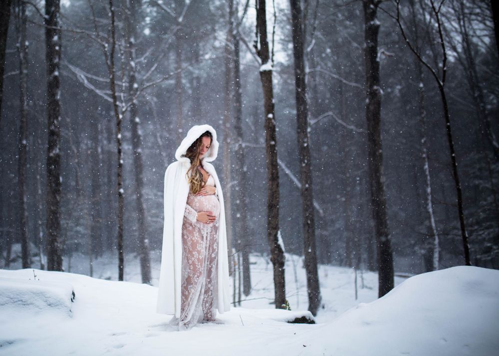 A figure in a flowing pink dress and white cape stands elegantly in a snowy winter forest setting.