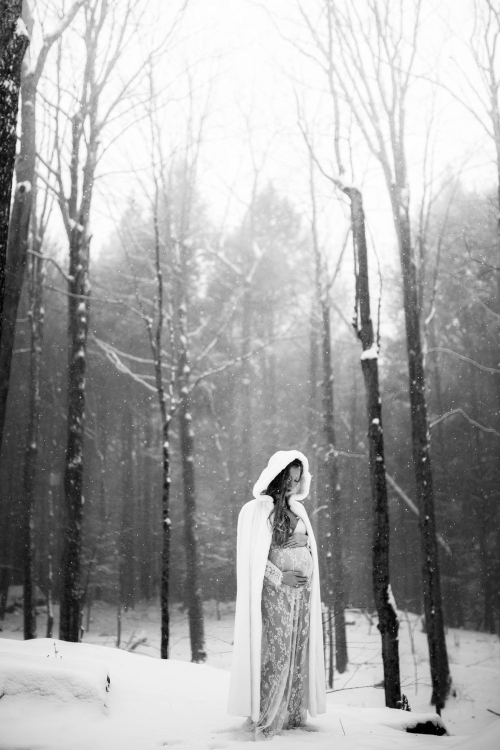 A ethereal winter portrait of a woman in a white cape standing among snowy trees.