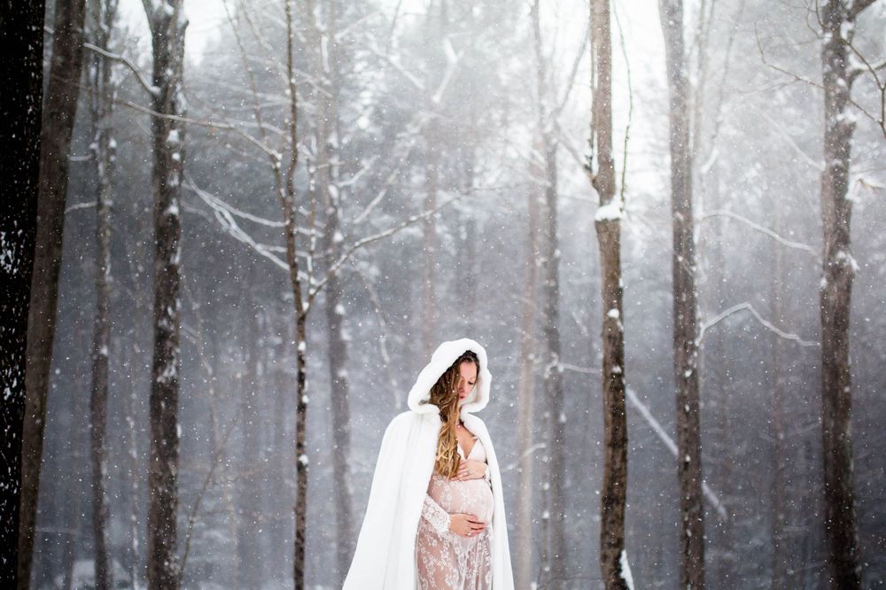 A delicate silhouette in a lace dress poses among snow-covered trees in a misty winter forest.