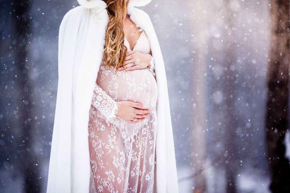 Close-up of a flowing pink lace dress and white cape with falling snow in a winter setting.
