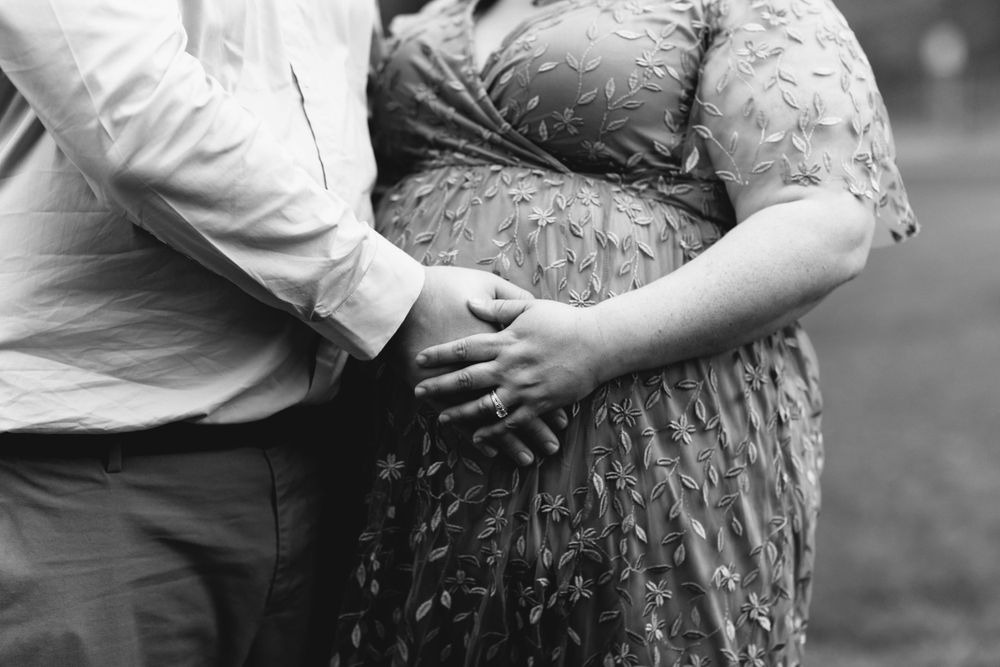 An intimate black and white detail shot of hands cradling a pregnant belly.
