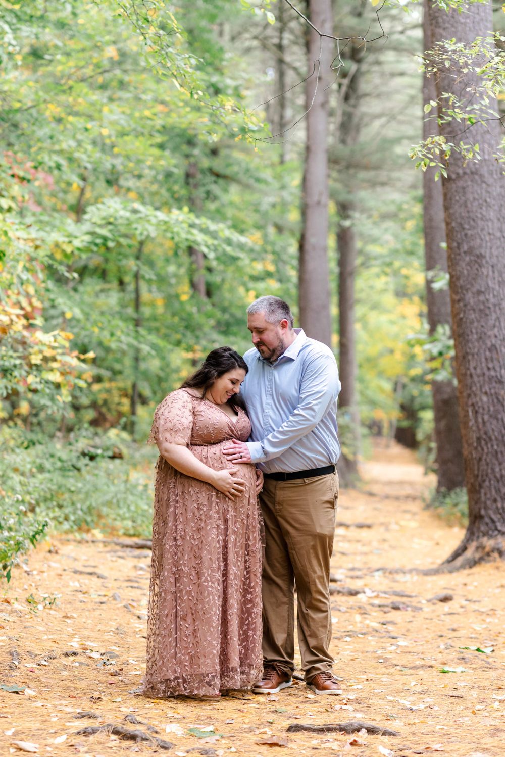 A tender maternity moment on a leaf-covered forest path during autumn.