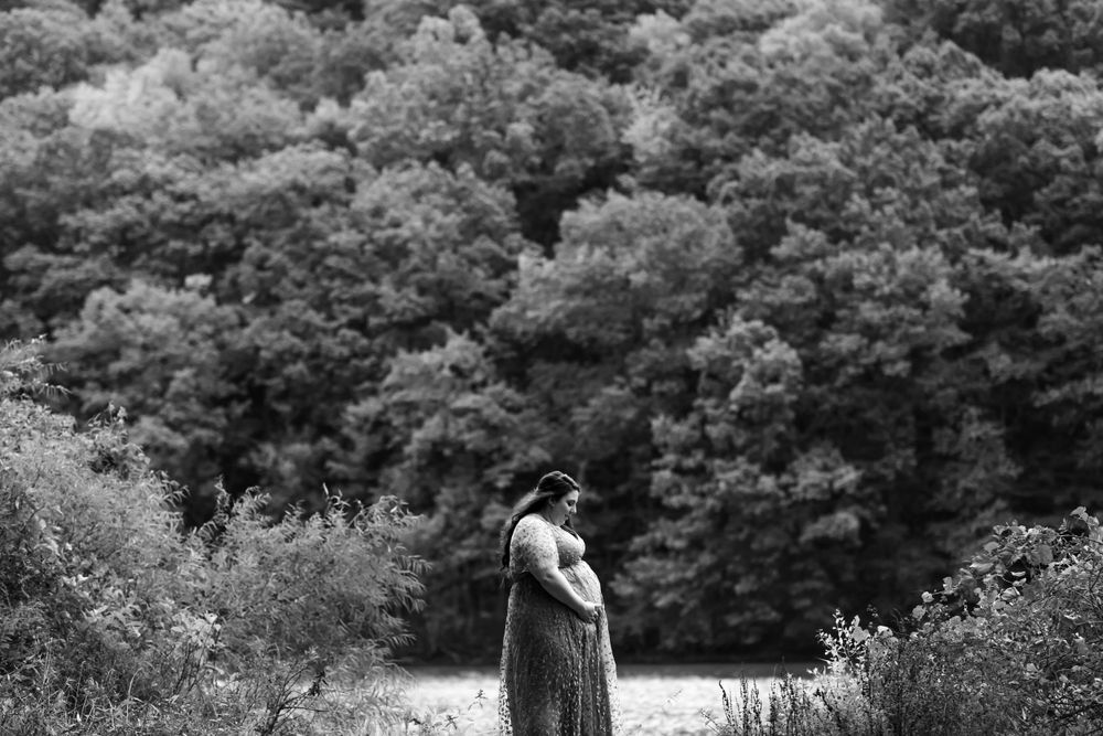 A black and white maternity portrait in a peaceful forest clearing.
