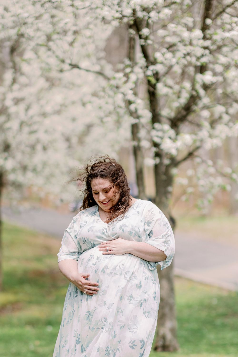 Maternity photos under blooming cherry blossoms with soft natural lighting.