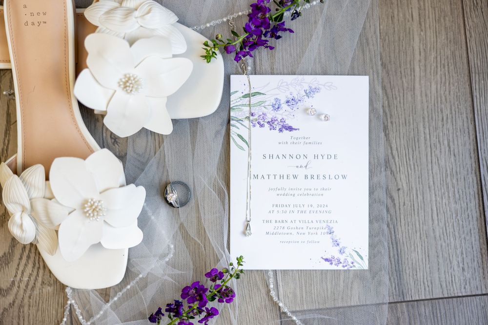 Wedding stationery with purple floral designs and white flowers arranged on rustic wood background.