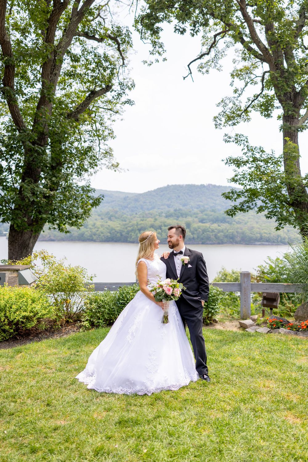 A wedding couple shares an intimate moment on a grassy hill overlooking a scenic lake with mountains in the background.