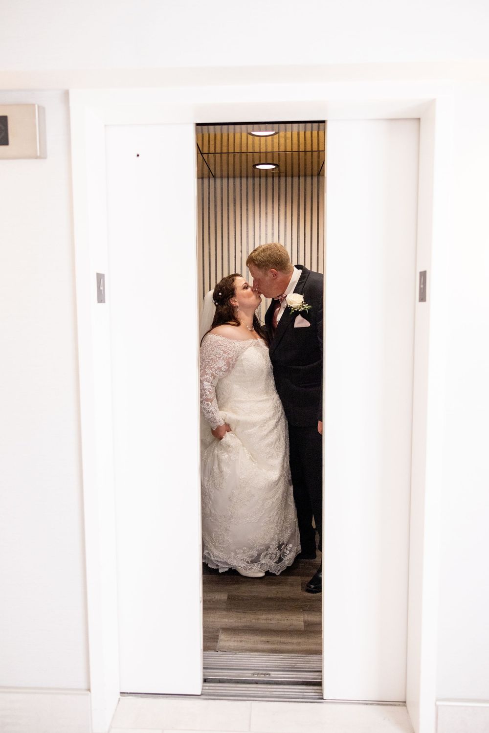 Wedding couple in formal attire walking through a bright white doorway or hallway.
