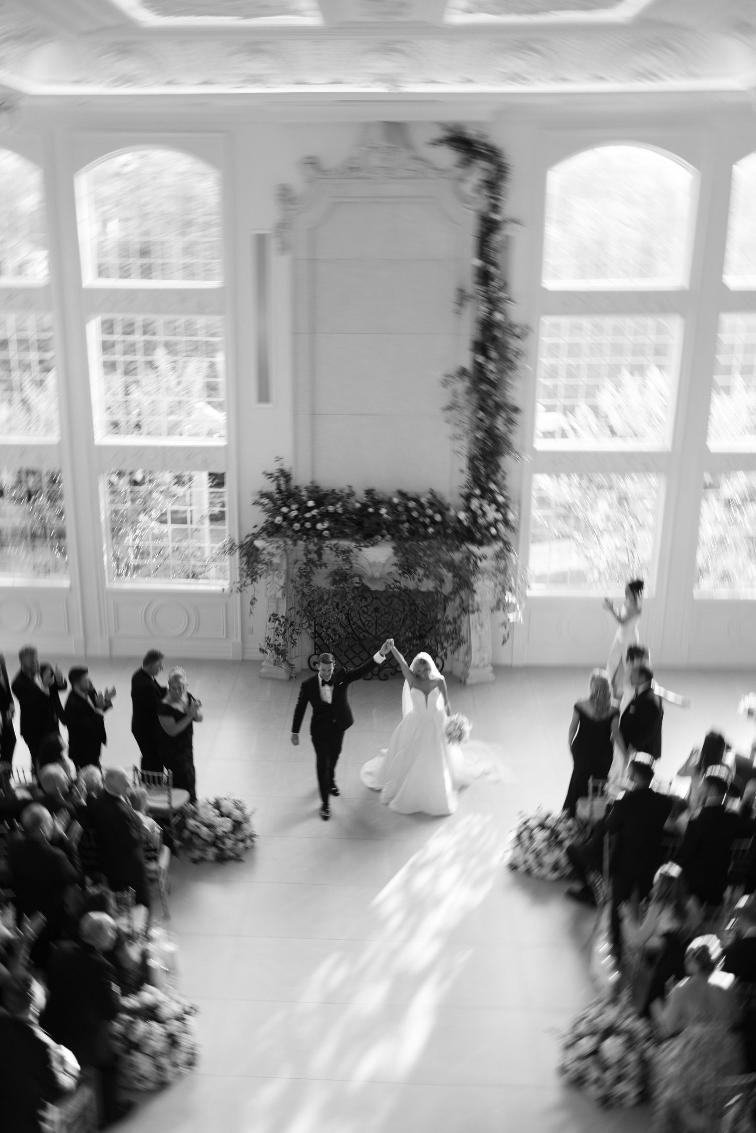 Aerial black and white photo of bride and groom celebrating at indoor wedding ceremony.
