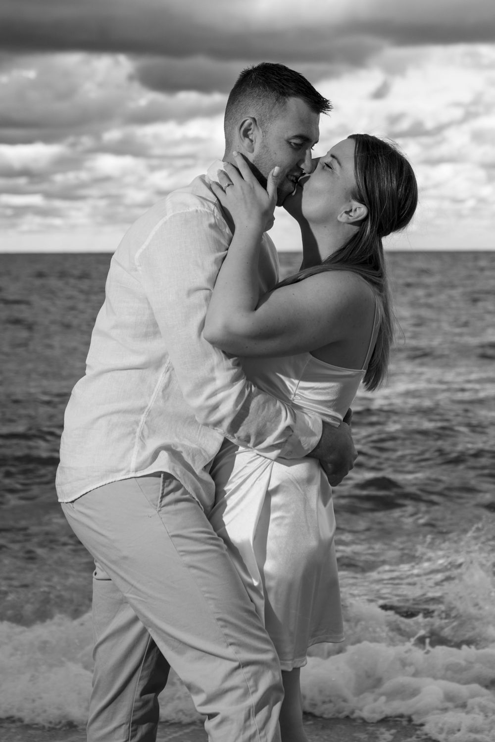 Engaged couple embracing on a Fort Lauderdale beach in black and white kissing with the ocean and sunset
