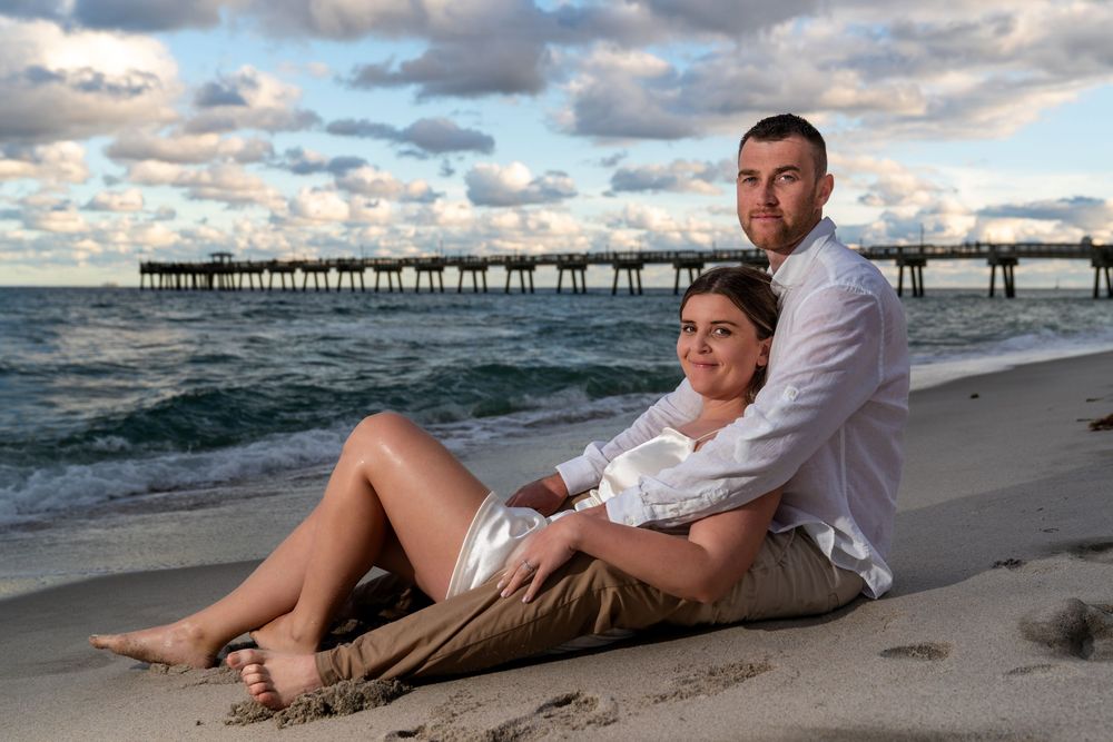 Elopement couple embracing on a Fort Lauderdale beach at sunset, looking at each other with ocean waves and dramatic clouds in the back