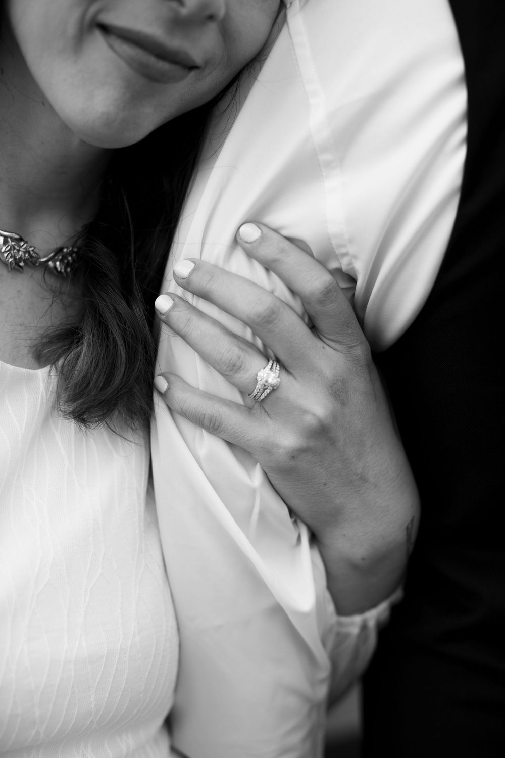 Black and white photo of a bride resting her hand on a groom's chest, showcasing her diamond wedding ring set.