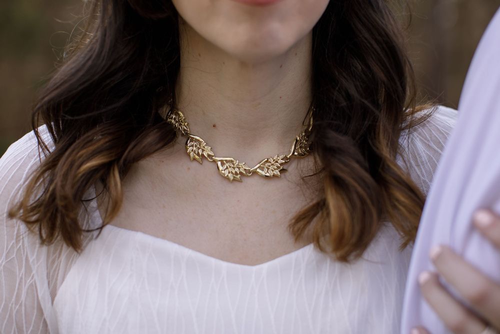 Woman wearing an elegant gold leaf branch choker necklace with a white dress in an outdoor setting.