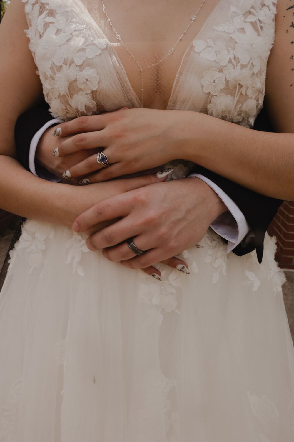 Close-up of wedding rings and hands with lace wedding dress detail.