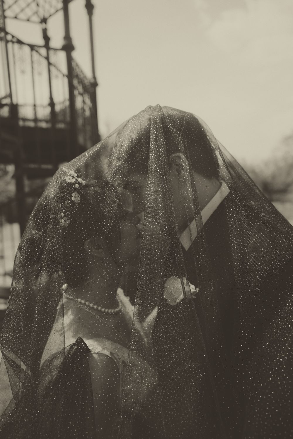 An artistic black and white photo of a couple beneath a delicate veil.