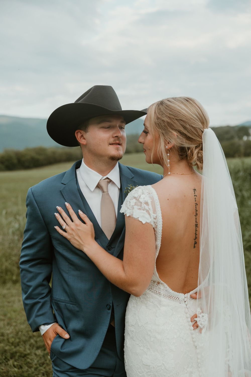 Couple in western-inspired wedding attire share an intimate moment against mountain backdrop.