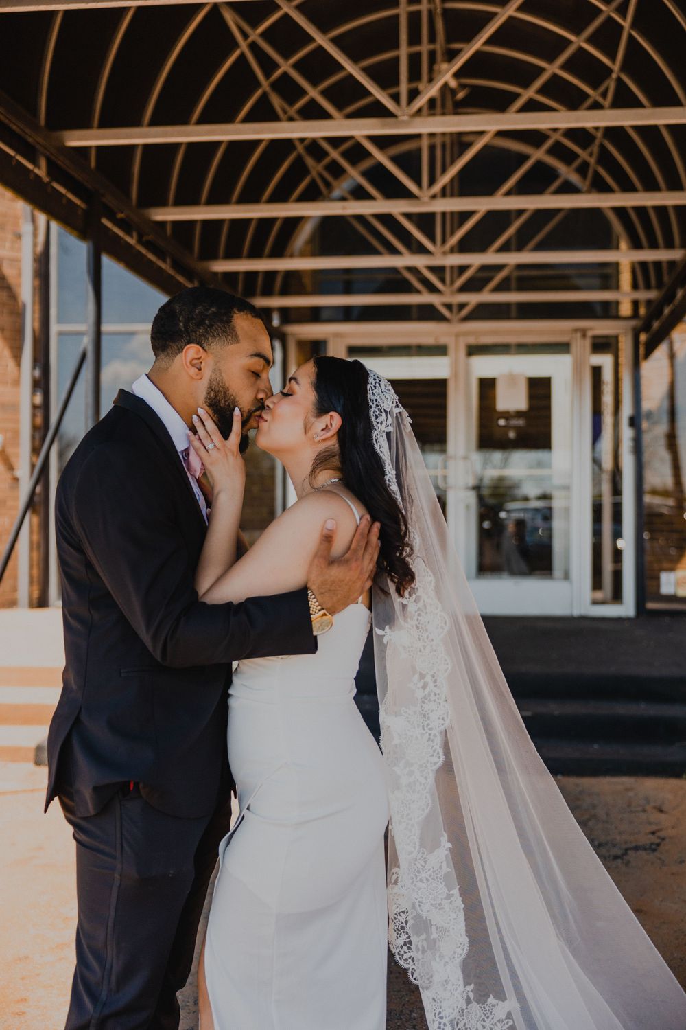 Romantic wedding portrait of couple embracing under architectural covered walkway at sunset.