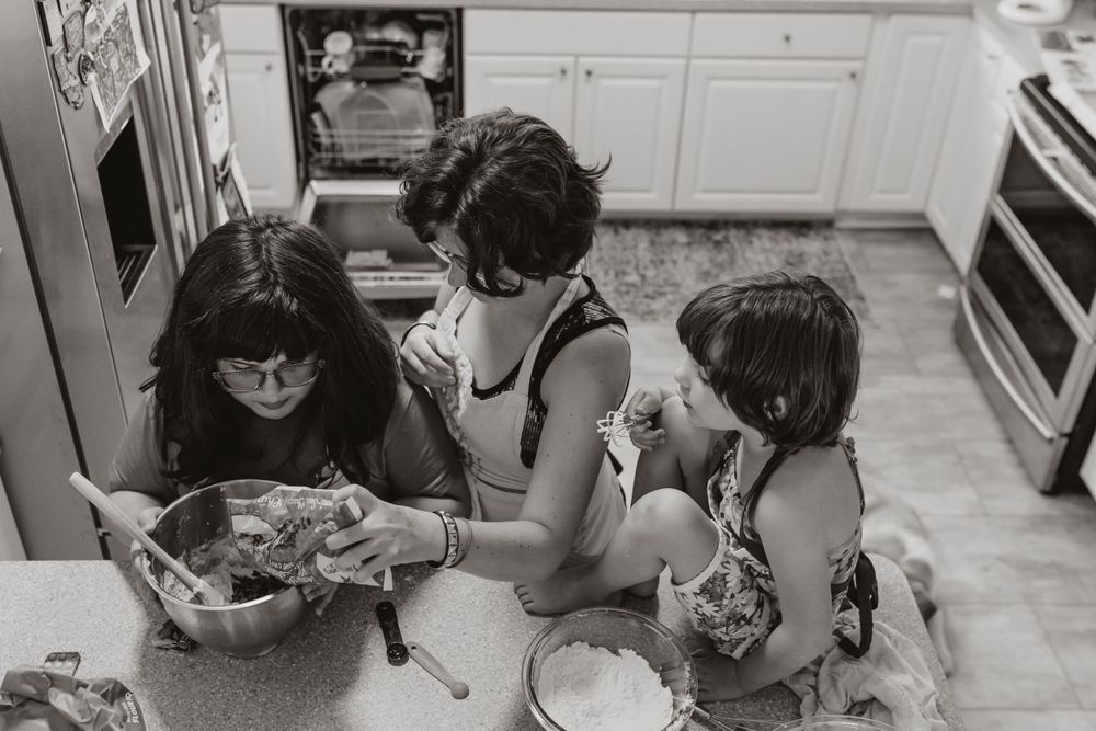 A black and white overhead view of three people sitting at a kitchen counter eating snacks together.