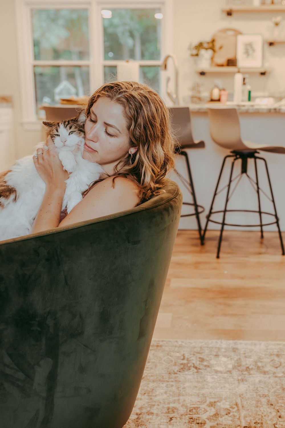 A relaxed woman lounges in a dark green velvet chair while snuggling her cat. Whitney Popp, Phoenix AZ photographer.