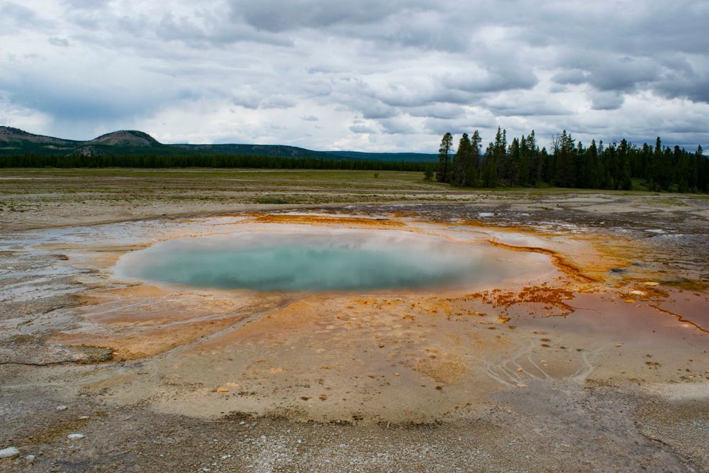 Turquoise hot spring pool surrounded by orange mineral deposits in Yellowstone's geothermal basin.