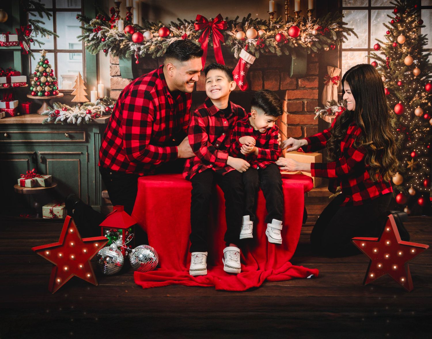 Happy family of four in matching red plaid shirts posing together in Christmas holiday photo session.