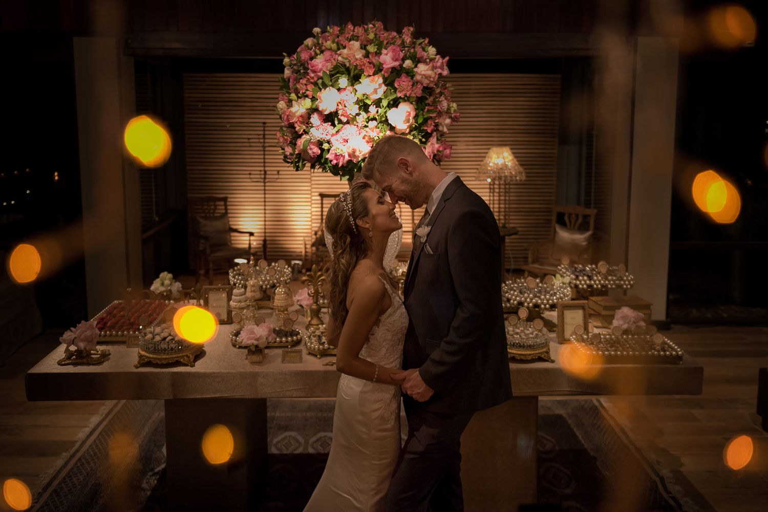 A romantic moment shared on a dance floor with pink floral decor and warm bokeh lighting.