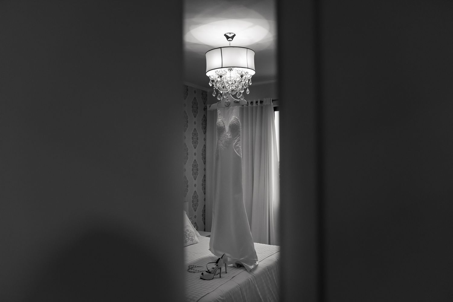 A wedding dress hangs in doorway silhouette beneath an elegant chandelier.