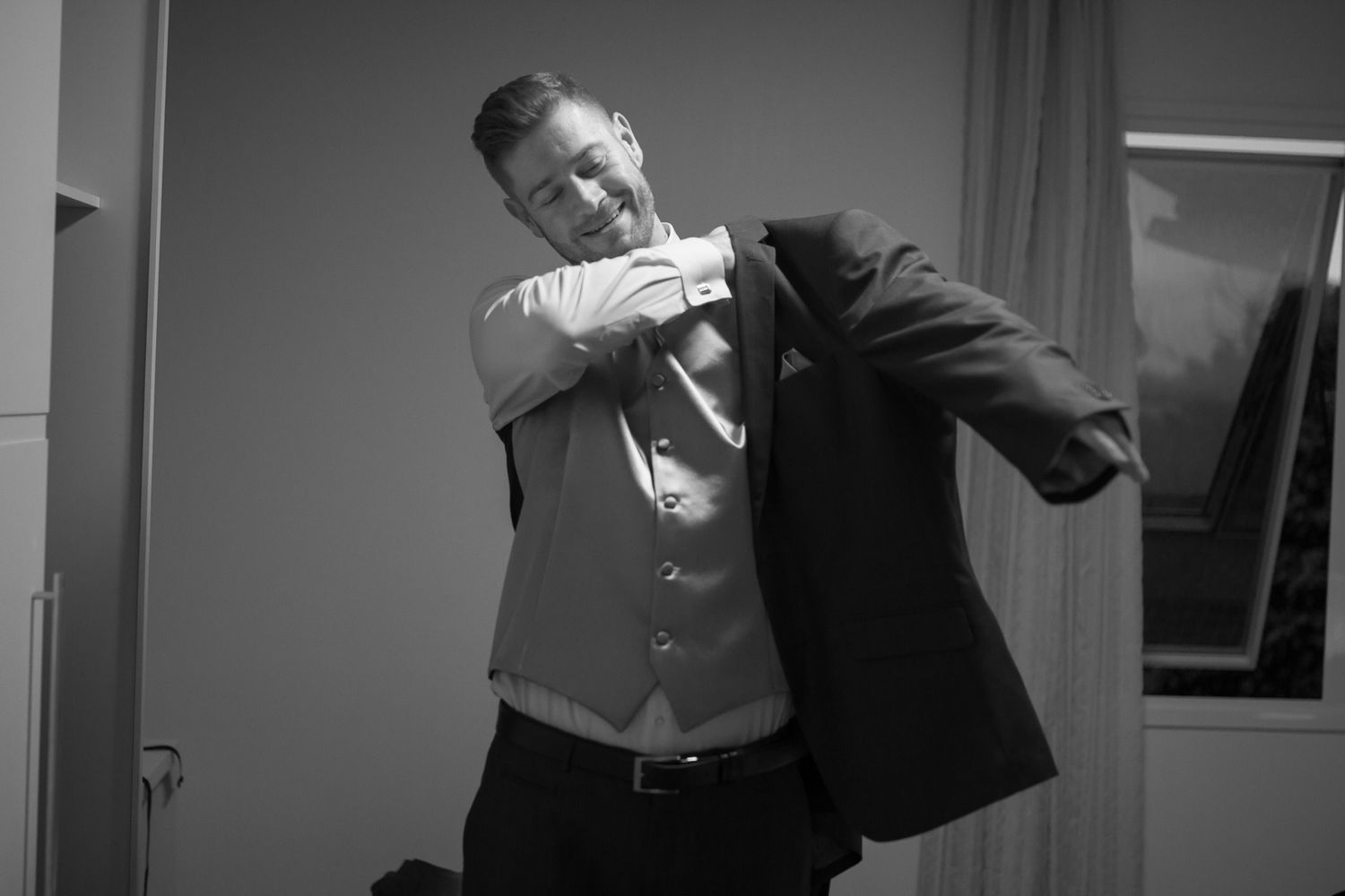 Monochrome portrait of someone putting on a suit jacket indoors.