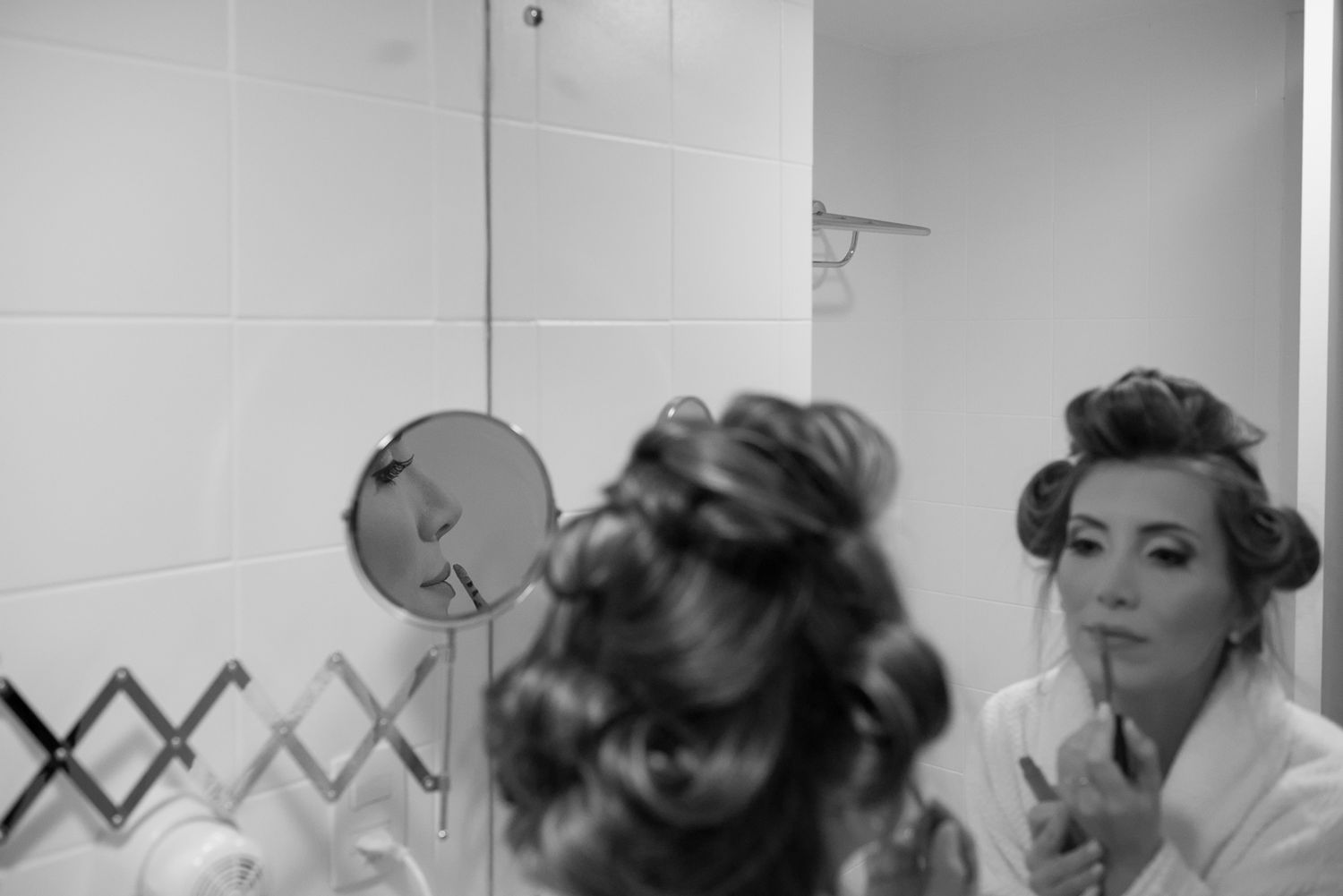 Women with hair in rollers preparing in front of bathroom mirror.