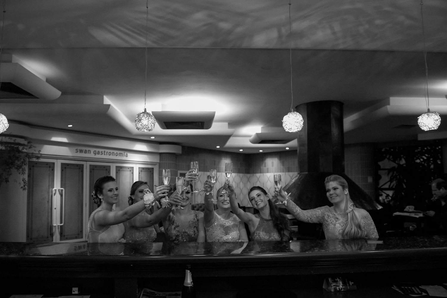 Wedding party celebrates with drinks at bar in black and white photograph.