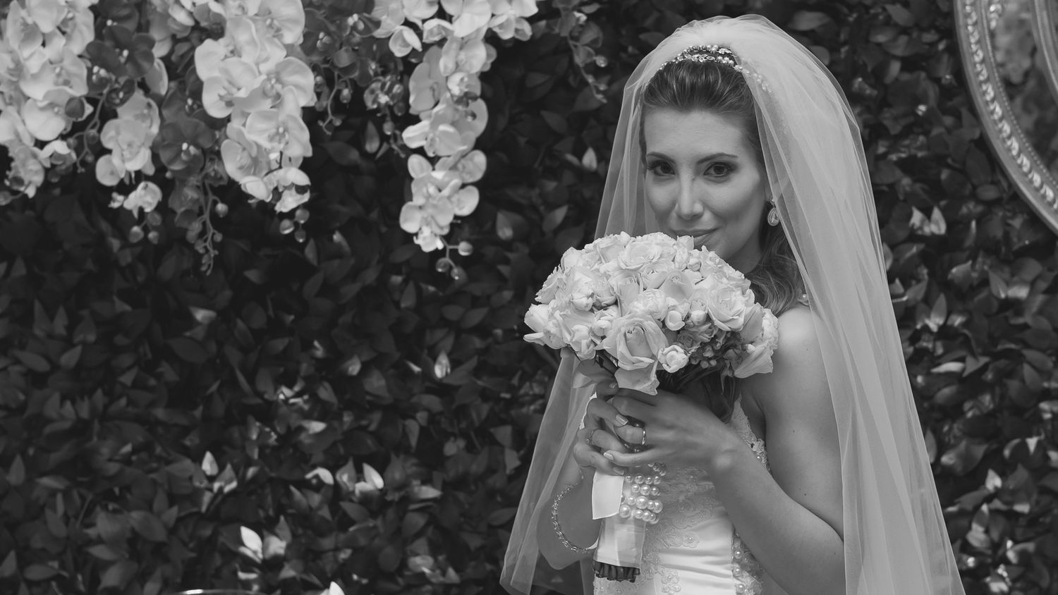 A bridal portrait showing a white dress and delicate veil with a floral bouquet against a garden backdrop.