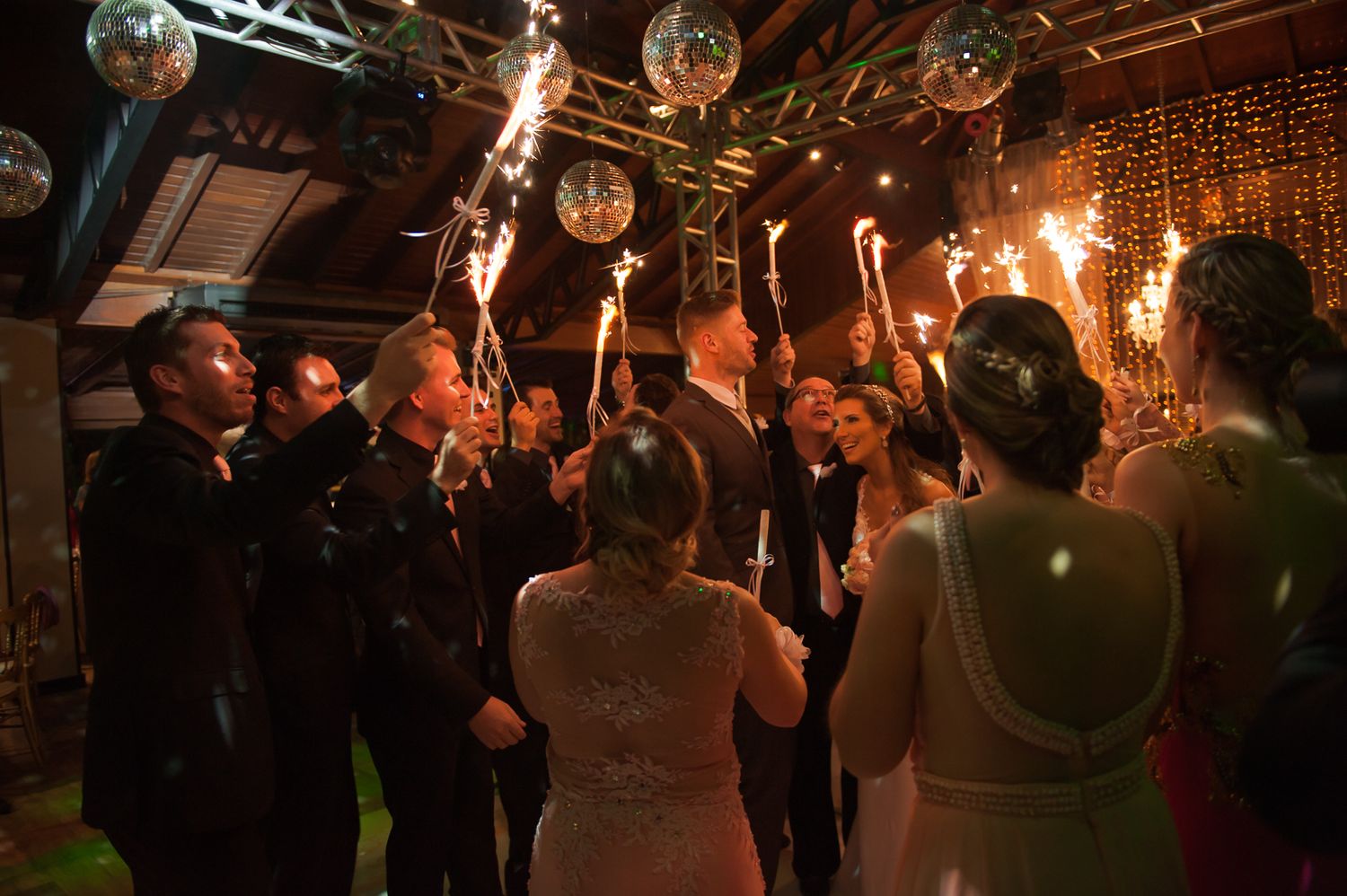 Wedding guests dancing and celebrating under disco balls and string lights.