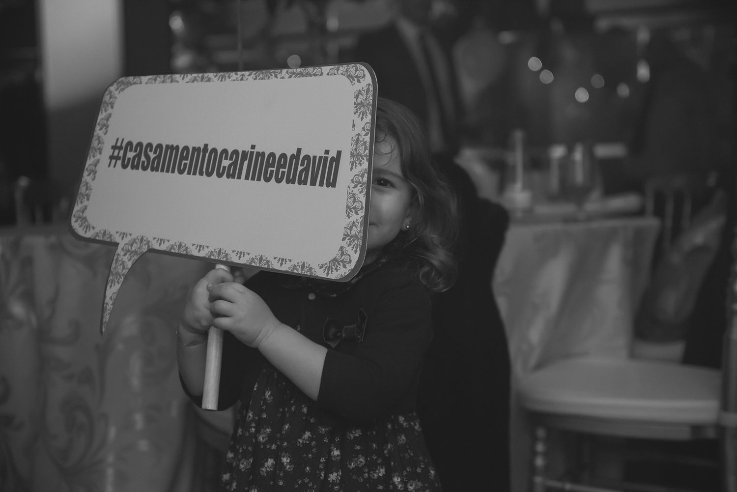 A black and white photo of someone holding a social media hashtag sign at a wedding celebration.
